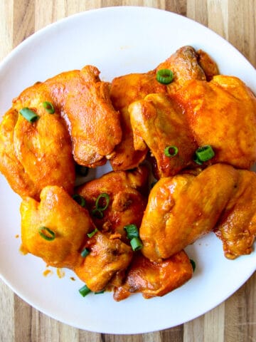 Chicken thighs on a white plate garnished with green onions.