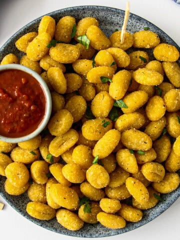 Air fryer gnocchi on a blue plate with a small bowl of marinara dip.