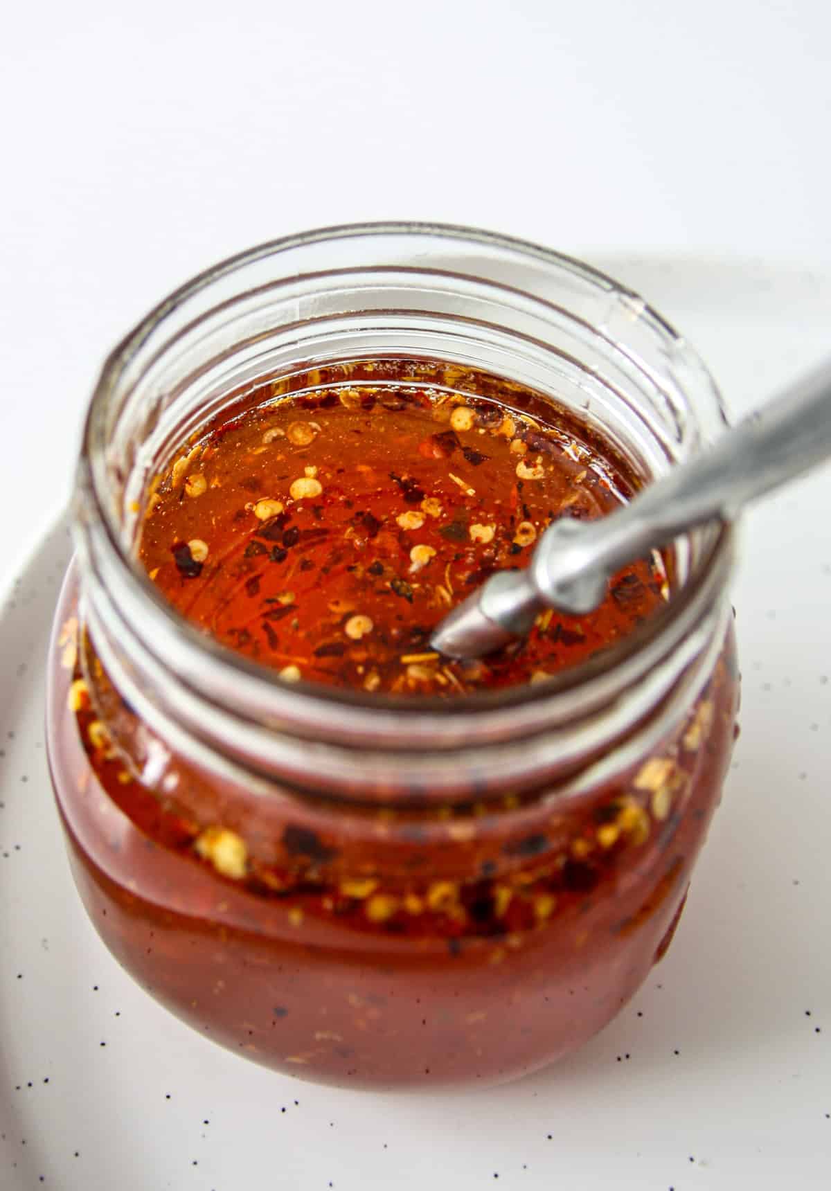 Hot honey sauce in a glass jar with a spoon inserted.